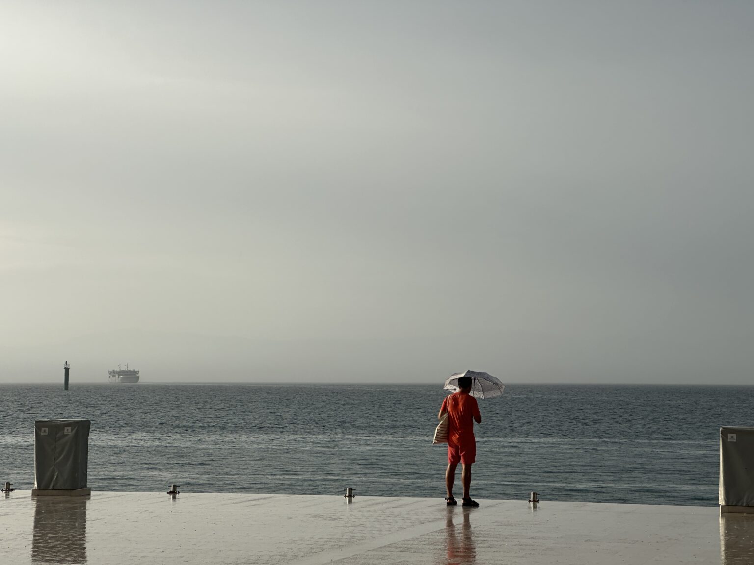 Čovek sa kišobranom čeka trajekt na molu.